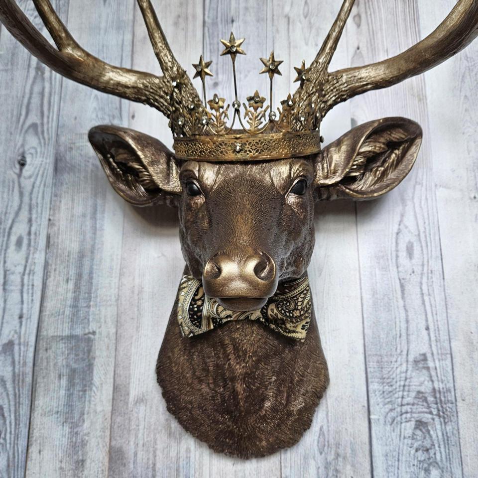 Faux taxidermy deer head wall mount with crown and bow tie.