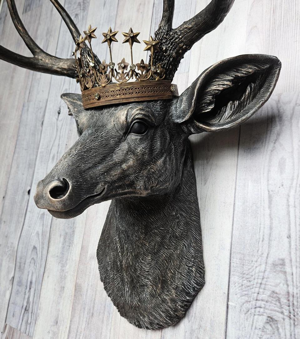 Faux taxidermy deer head wall mount. The head and antlers are black with dark copper accents. The deers head has additional accents in antique white, the eyes are black.A rustic vintage inspired star Santos crown sites atop the deers head