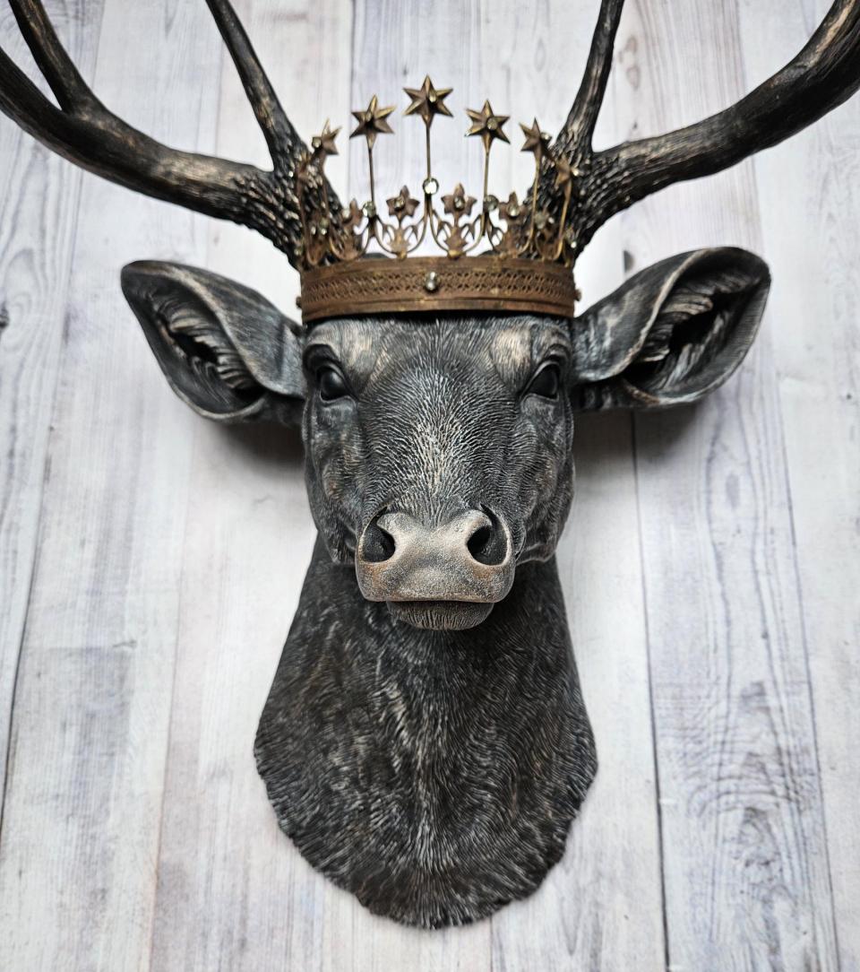 Faux taxidermy deer head wall mount. The head and antlers are black with dark copper accents. The deers head has additional accents in antique white, the eyes are black.A rustic vintage inspired star Santos crown sites atop the deers head