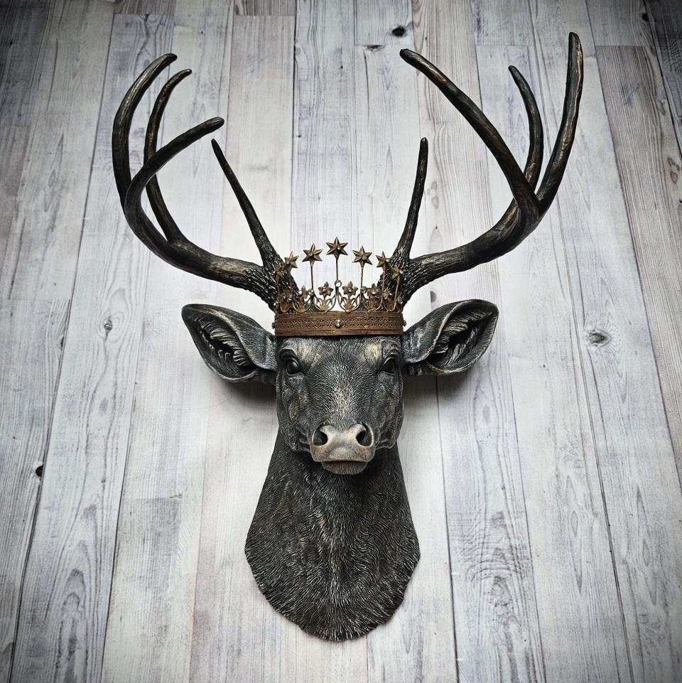 Faux taxidermy deer head wall mount. The head and antlers are black with dark copper accents. The deers head has additional accents in antique white, the eyes are black.A rustic vintage inspired star Santos crown sites atop the deers head.