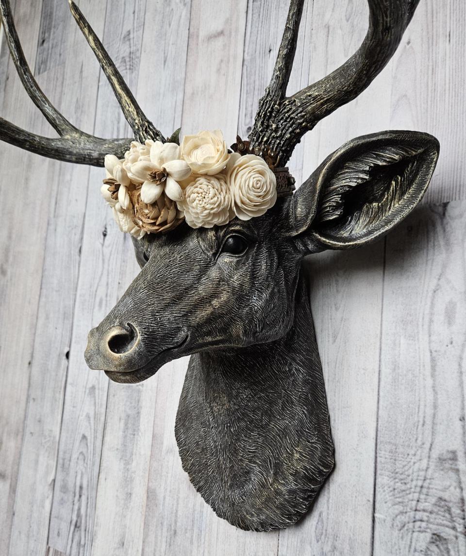 faux taxidermy deer head, painted chestnut brown with gold and antique white accents. The antlers have been painted in the same color combination. A floral crown made of cream and natural bark sola flowers rests atop the deers head.