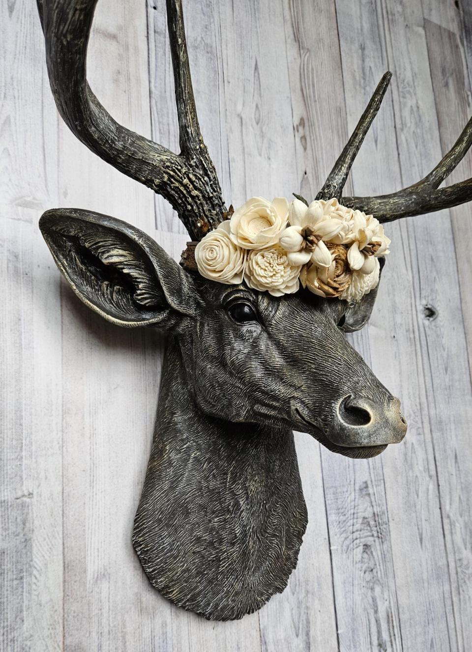 faux taxidermy deer head, painted chestnut brown with gold and antique white accents. The antlers have been painted in the same color combination. A floral crown made of cream and natural bark sola flowers rests atop the deers head.
