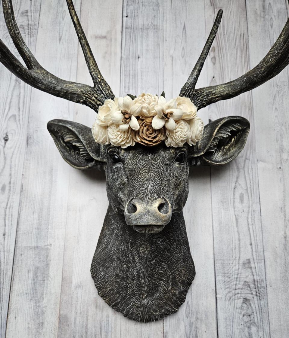 faux taxidermy deer head, painted chestnut brown with gold and antique white accents. The antlers have been painted in the same color combination. A floral crown made of cream and natural bark sola flowers rests atop the deers head.