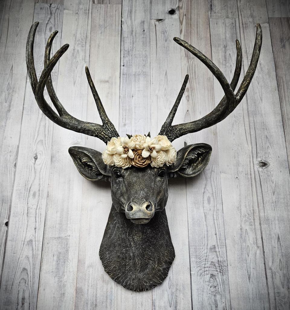 faux taxidermy deer head, painted chestnut brown with gold and antique white accents. The antlers have been painted in the same color combination. A floral crown made of cream and natural bark sola flowers rests atop the deers head.