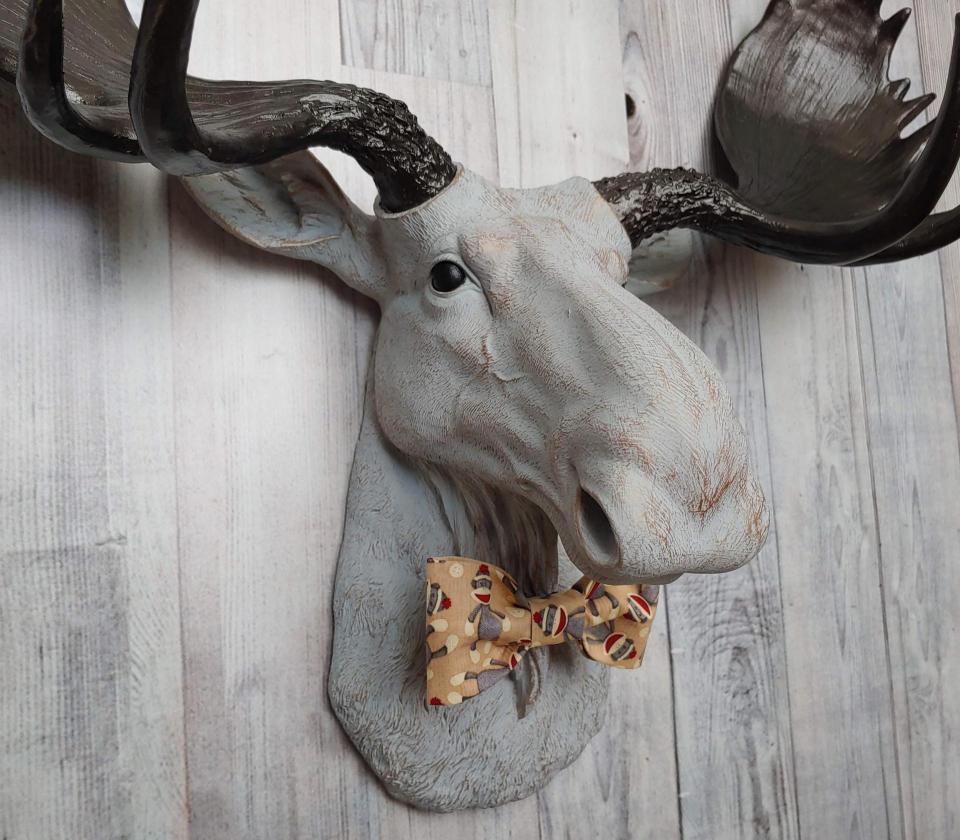 Faux taxidermy  moose head, painted pale grey with bronze accenting. Antlers are painted rubbed bronze. A removable sock monkey print bow tie accents the moose's neck.
