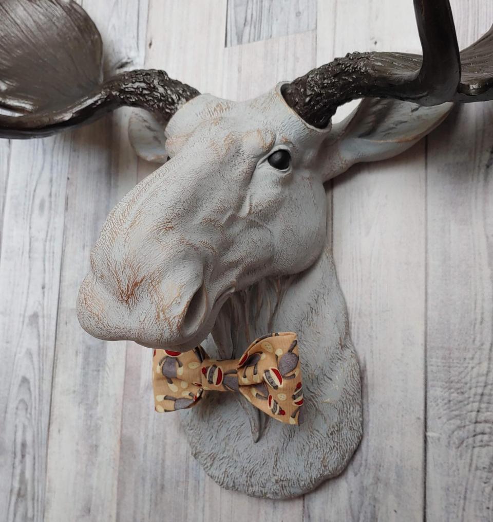 Faux taxidermy  moose head, painted pale grey with bronze accenting. Antlers are painted rubbed bronze. A removable sock monkey print bow tie accents the moose's neck.