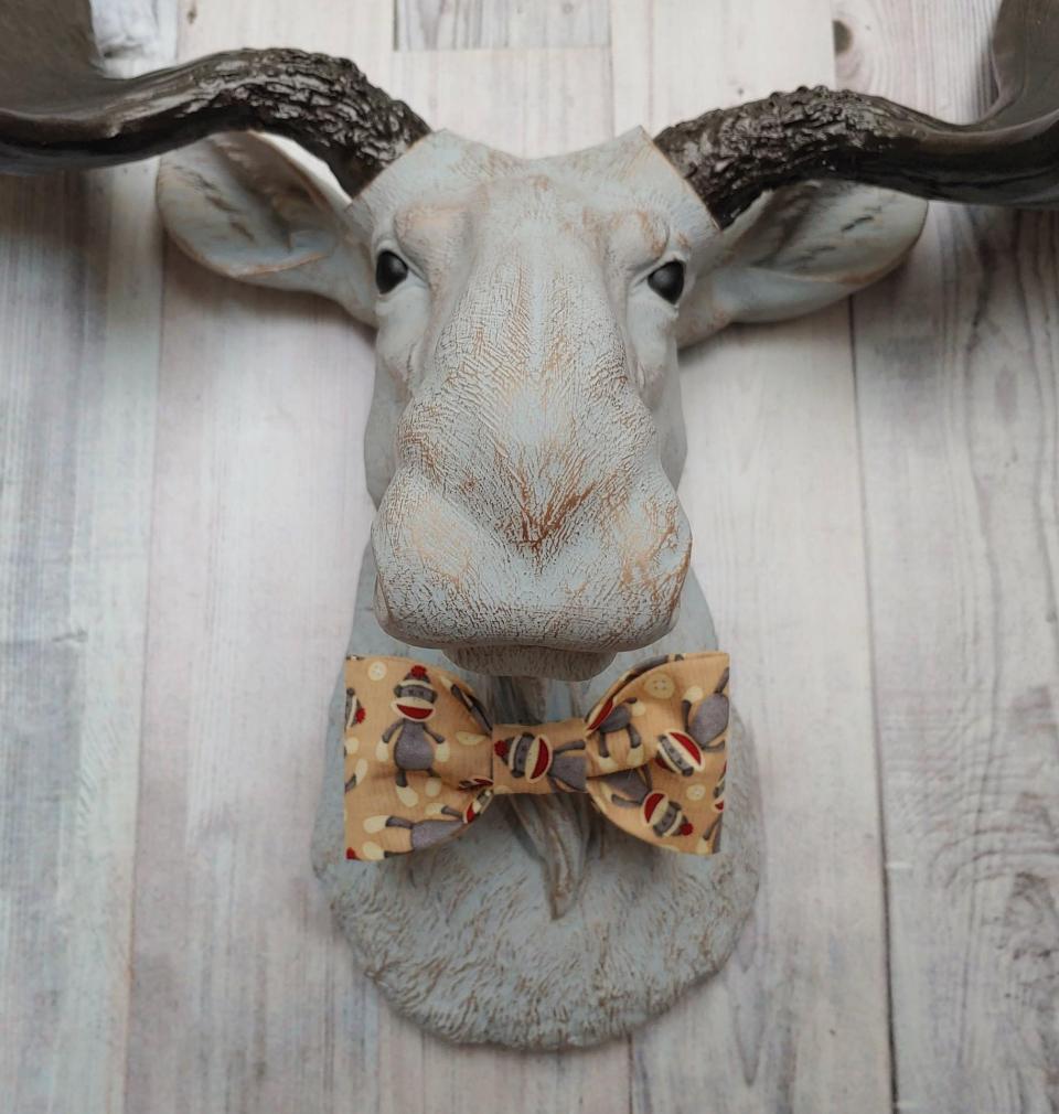 Faux taxidermy  moose head, painted pale grey with bronze accenting. Antlers are painted rubbed bronze. A removable sock monkey print bow tie accents the moose's neck.
