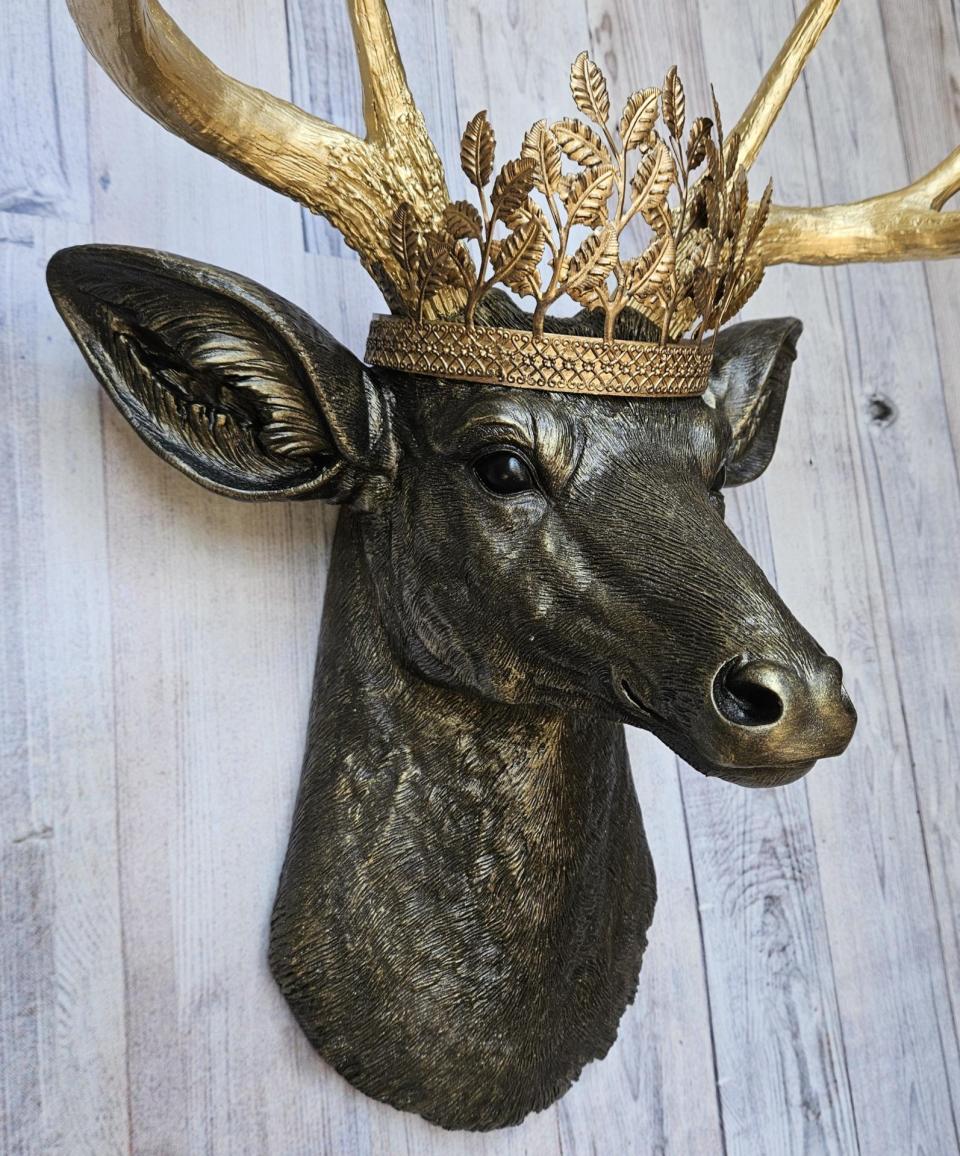 Faux taxidermy deer head wall mount, painted rubbed bronze with gold antlers and gold accents. A metal leaf work gold crown rests atop the deers head.