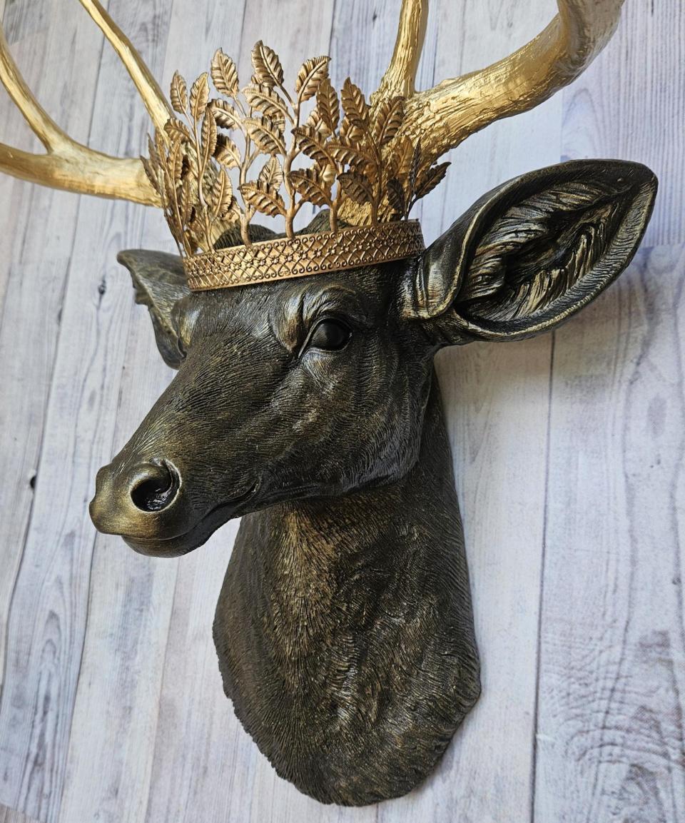 Faux taxidermy deer head wall mount, painted rubbed bronze with gold antlers and gold accents. A metal leaf work gold crown rests atop the deers head.