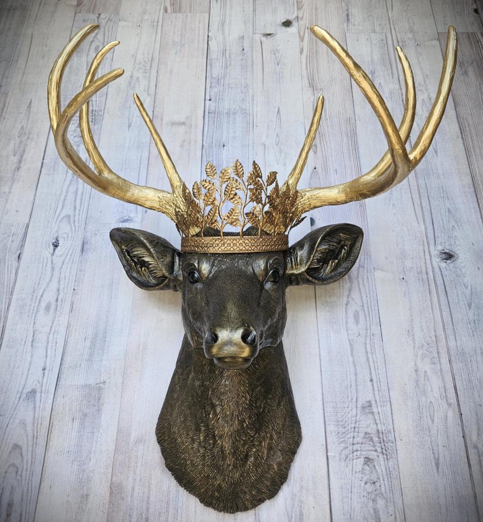 Faux taxidermy deer head wall mount, painted rubbed bronze with gold antlers and gold accents. A metal leaf work gold crown rests atop the deers head.