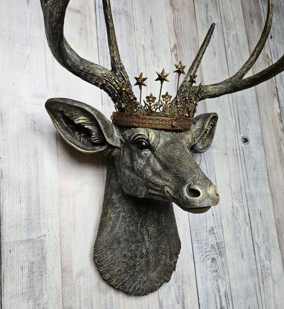 faux taxidermy deer head that's been painted chestnut brown with gold and antique white accents, the antlers are painted in the same color combination. A vintage bronze Santos metal crown with rhinestones accents the top of the deers head.