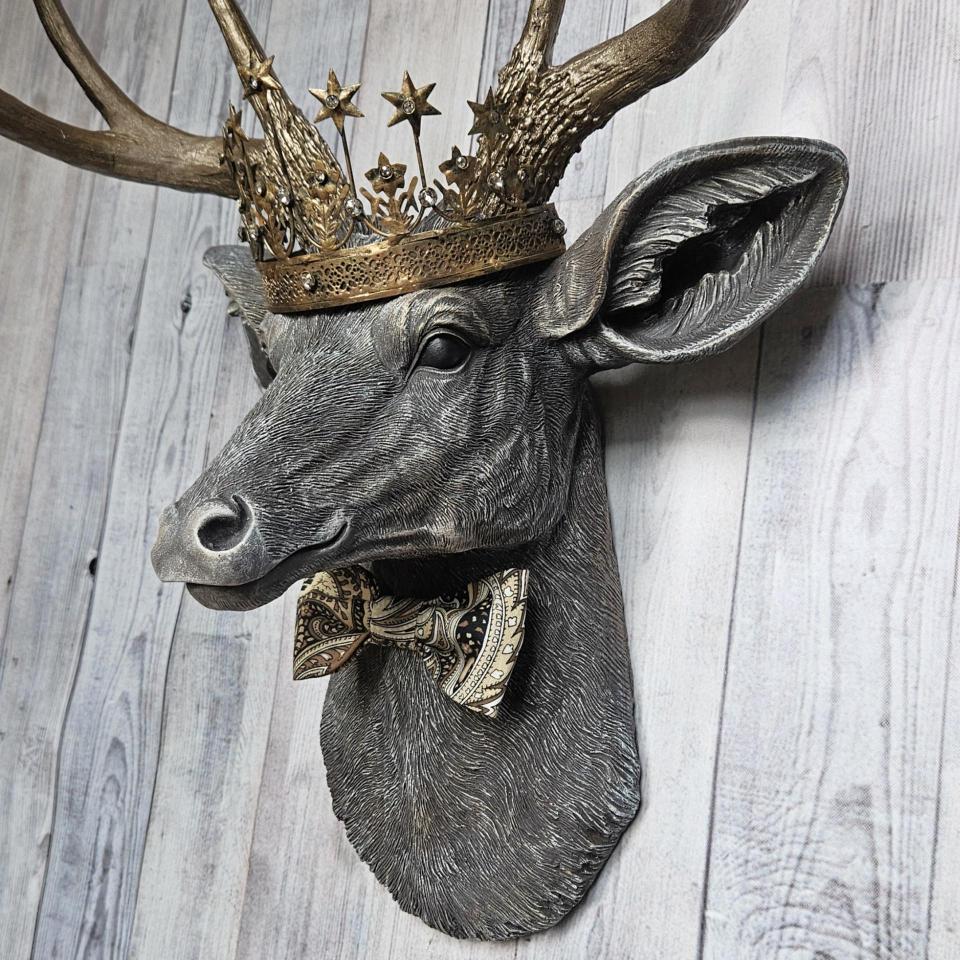 Faux taxidermy deer head wall mount with crown and bow tie.