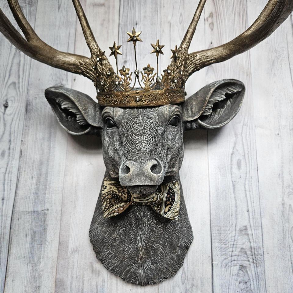 Faux taxidermy deer head wall mount with crown and bow tie.