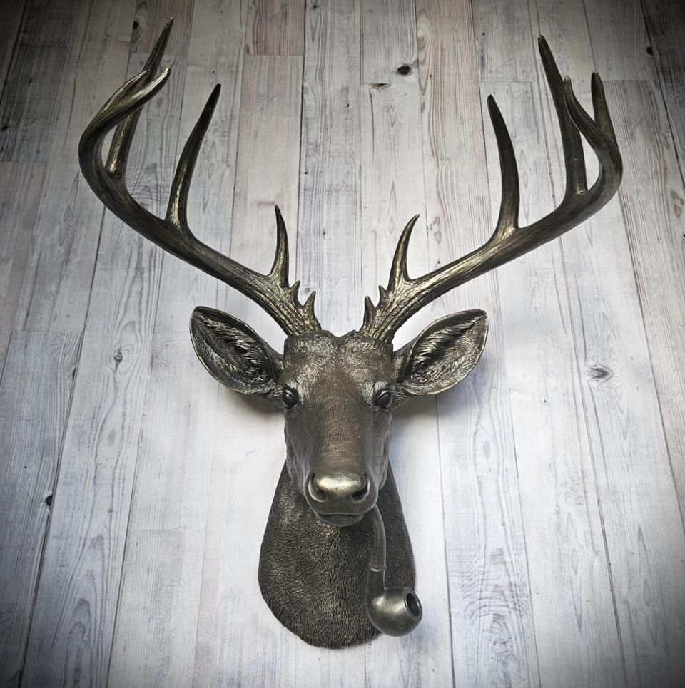 Rubbed bronze faux taxidermy deer head with gold accents. A smoking pipe extends from the deers mouth.