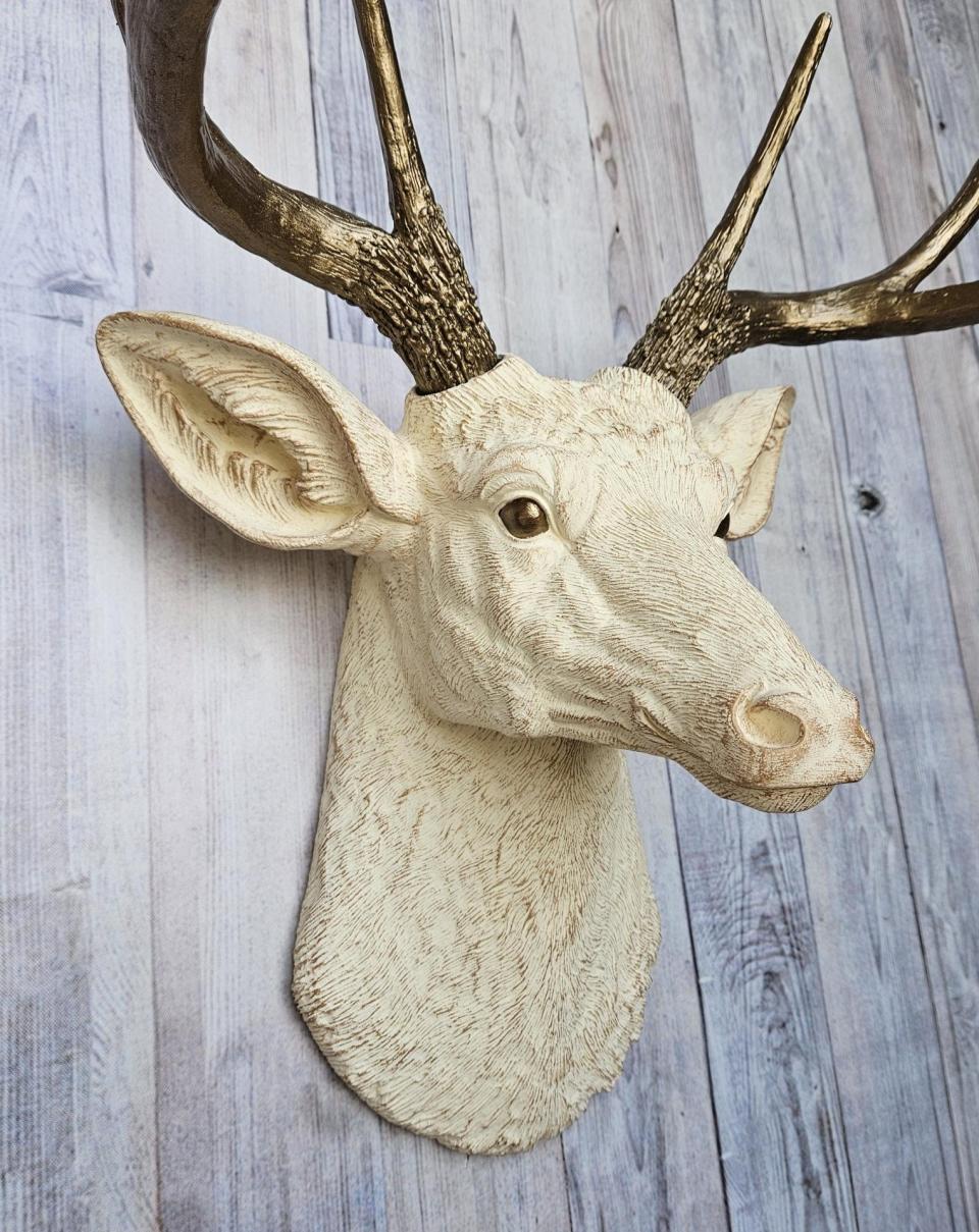 Faux taxidermy deer head, painted antique white with antique gold accenting. The antlers are antique gold a small brass bird is perched on the left facing antler.
