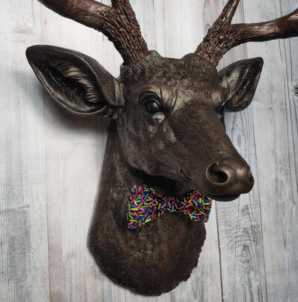 Faux taxidermy deer head, painted rubbed bronze with dark copper accenting on the head, antlers are dark copper. Removable bow tie, fabric is black with multi colored sprinkles.