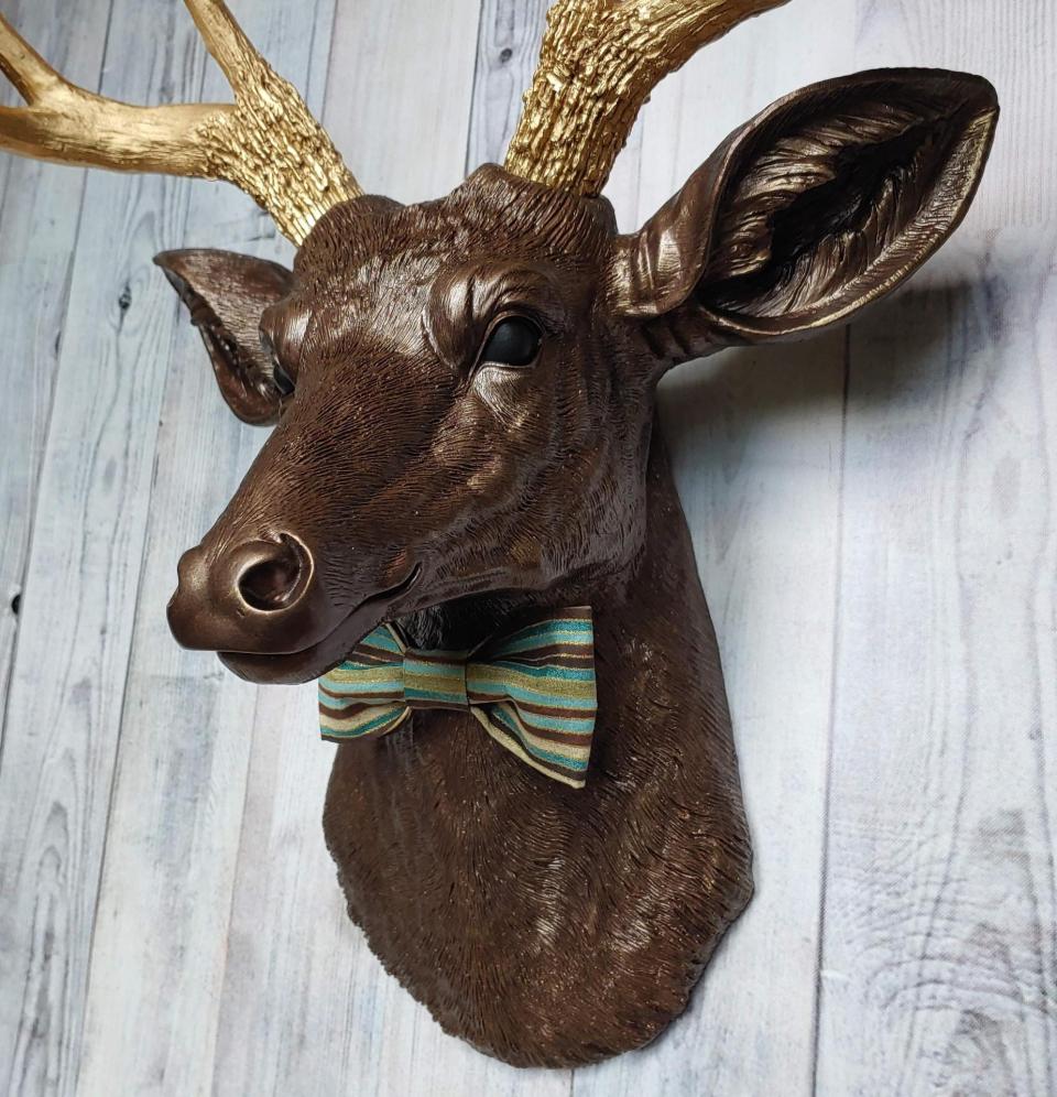 Faux taxidermy deer head painted dark copper with gold accents and gold antlers. A striped bow tie is at the neck.