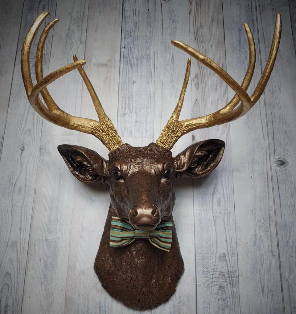 Faux taxidermy deer head painted dark copper with gold accents and gold antlers. A striped bow tie is at the neck.