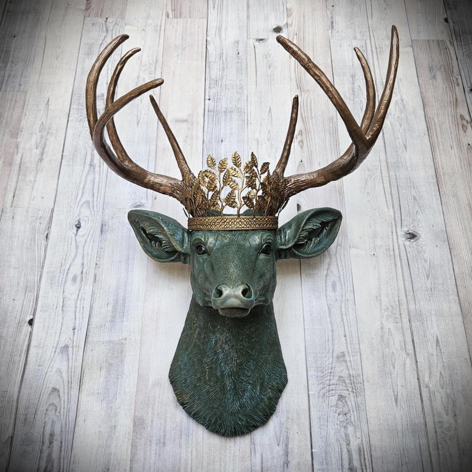 Faux taxidermy deer head wall mount, head is painted verdigris with antique gold antlers. A metal leaf crown rests atop the deers head.