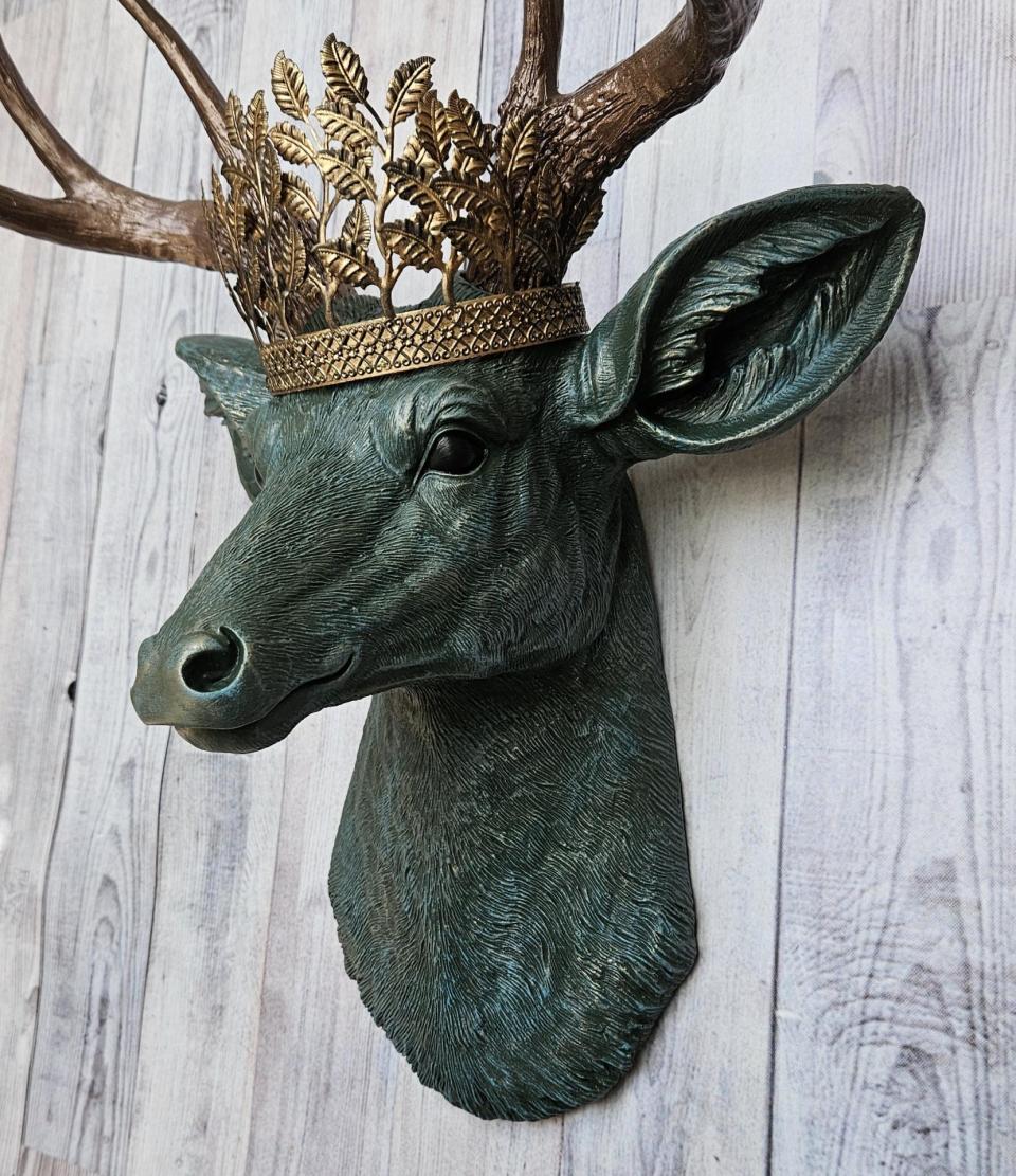 Faux taxidermy deer head wall mount, head is painted verdigris with antique gold antlers. A metal leaf crown rests atop the deers head