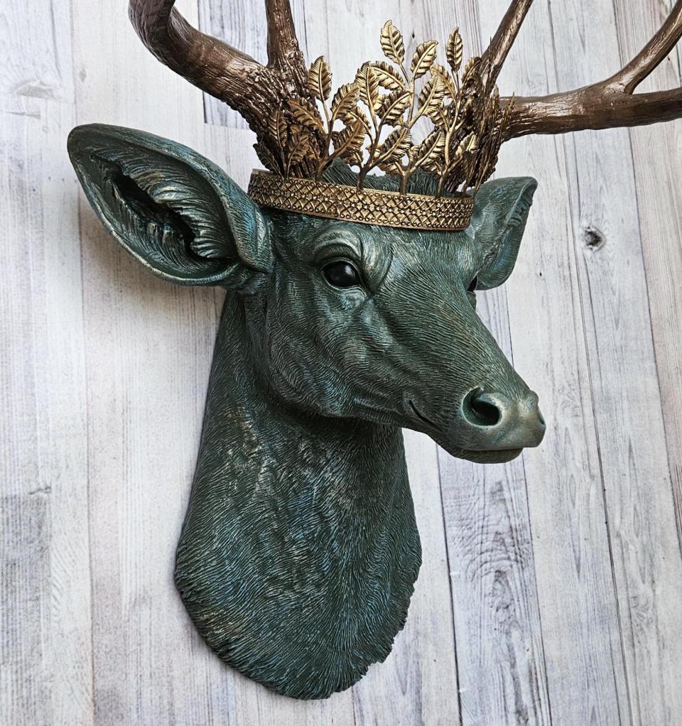 Faux taxidermy deer head wall mount, head is painted verdigris with antique gold antlers. A metal leaf crown rests atop the deers head