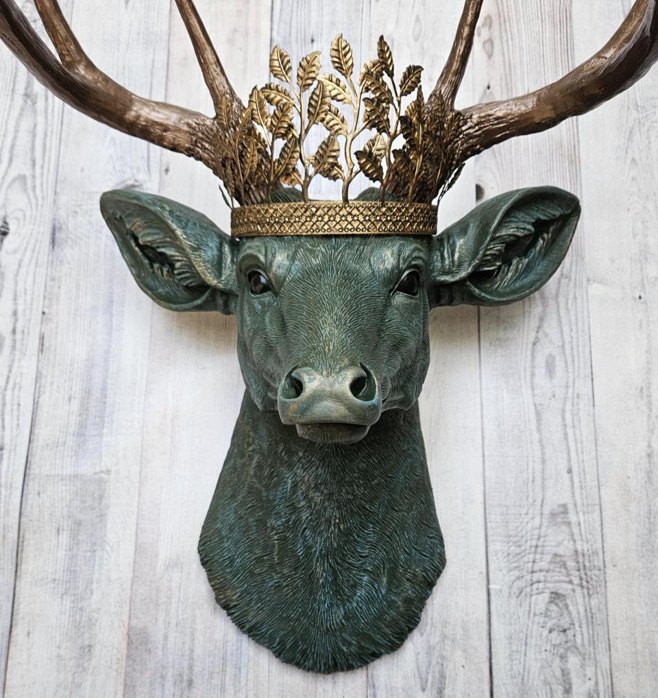 Faux taxidermy deer head wall mount, head is painted verdigris with antique gold antlers. A metal leaf crown rests atop the deers head
