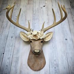 Faux taxidermy deer head, painted in natural colors with a brass bird on one antler and a wooden flower crown atop it's head.