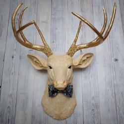 Faux taxidermy deer head painted cream with gold accenting and gold antlers. A fabric bow tie accents the neck, fabric color is dark blue multi with lighter blue and white.