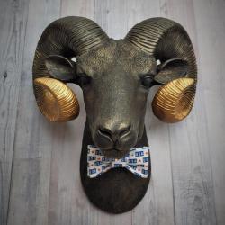 Faux taxidermy ram head wall mount, painted black with metallic gold tipped horns with graduating gold going to the head. A USA bow tie accents the neck of the ram.