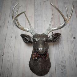 Faux taxidermy deer head painted rubbed bronze with silver accents and silver antlers. The deer has a bow tie on it's neck in black with colorful sprinkles.