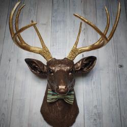Faux taxidermy deer head painted dark copper with gold accents and gold antlers. A striped bow tie is at the neck.