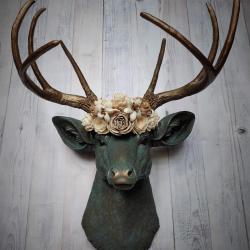 Faux taxidermy deer head painted verdigris with antique gold antlers. A floral crown made of cream sola flowers rests atop the deers head.