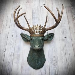 Faux taxidermy deer head wall mount, head is painted verdigris with antique gold antlers. A metal leaf crown rests atop the deers head.