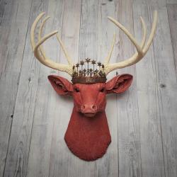 Faux taxidermy deer head, painted red with antique white antlers with a bronze Santos crown atop its head.