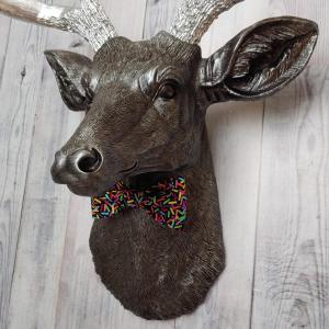 Faux taxidermy deer head painted rubbed bronze with silver accents and silver antlers. The deer has a bow tie on it's neck in black with colorful sprinkles.