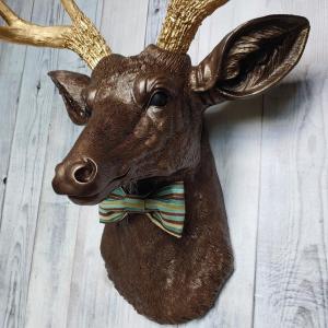 Faux taxidermy deer head painted dark copper with gold accents and gold antlers. A striped bow tie is at the neck.
