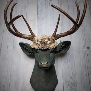 Faux taxidermy deer head painted verdigris with antique gold antlers. A floral crown made of cream sola flowers rests atop the deers head.