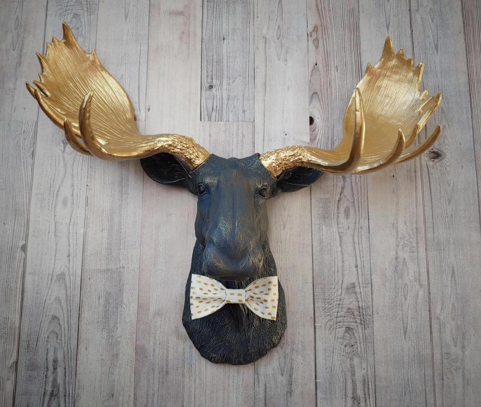 Faux taxidermy moose head painted midnight blue with metallic gold antlers. A white and gold polka dot bow tie accents the neck of the moose.