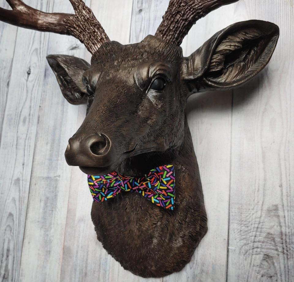 Faux taxidermy deer head, painted rubbed bronze with dark copper accenting on the head, antlers are dark copper. Removable bow tie, fabric is black with multi colored sprinkles.