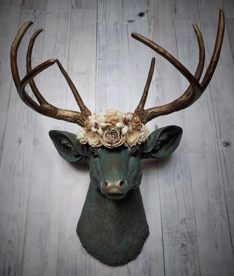 Faux taxidermy deer head painted verdigris with antique gold antlers. A floral crown made of cream sola flowers rests atop the deers head.